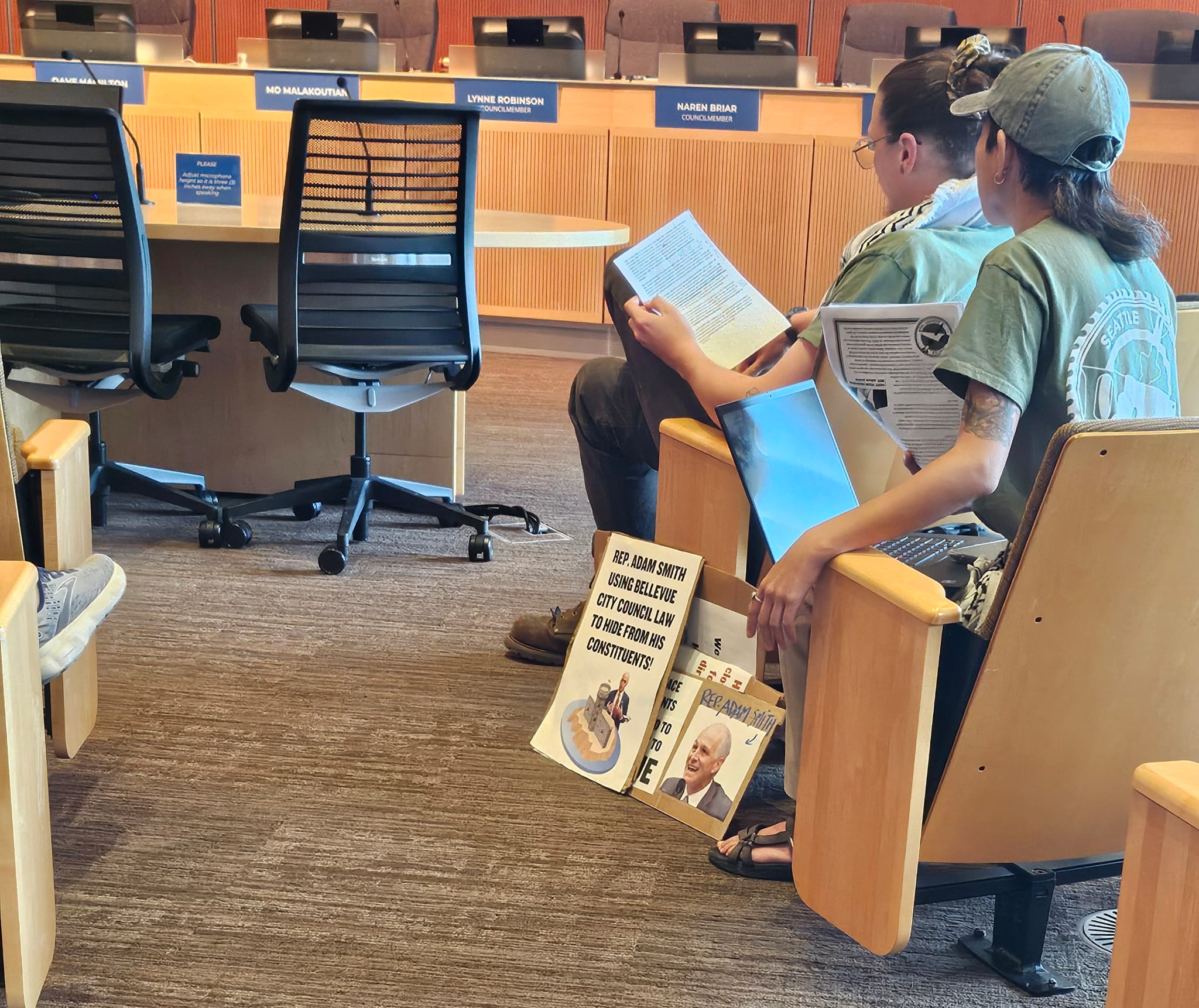 Members of Seattle Against War wait for a Bellevue City Council meeting to begin, bringing along signs opposing Rep. Adam Smith (D-Wash.) on May 12, 2025. Credit: Jessica Russak-Hoffman