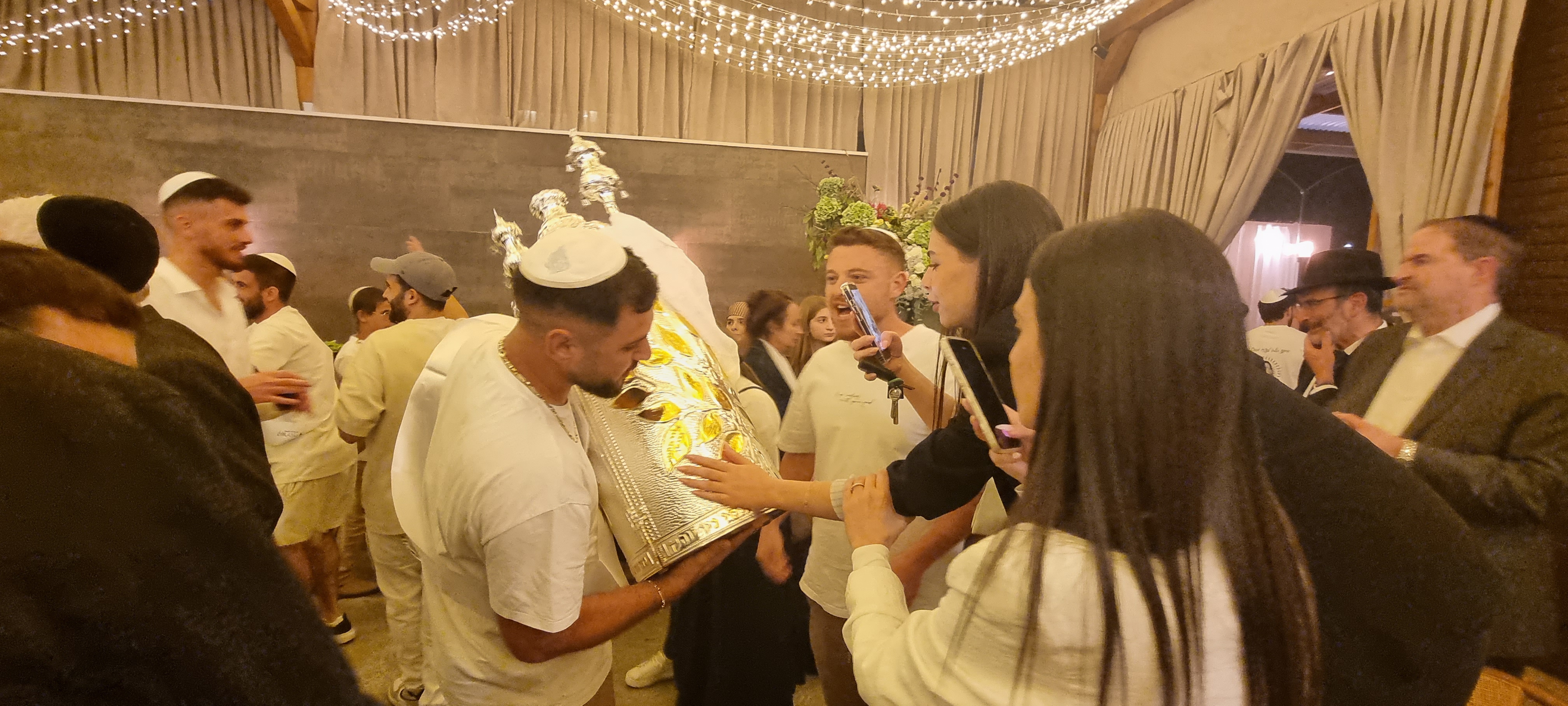 Celebrants at the David Castle event hall in Jerusalem photograph the names of friends murdered by Gazan terrorists on Oct. 7, 2023, engraved on a Torah scroll case, Oct. 3, 2026. Photo by Sharon Altshul.