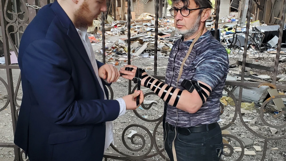 Sholom Ber Moskovitz, son of Rabbi Moshe and Miriam Moskovitz, leaders of the Jewish community in Kharkiv, wraps tefillin with a Jewish resident of the city, May 31, 2022. Credit: Courtesy.