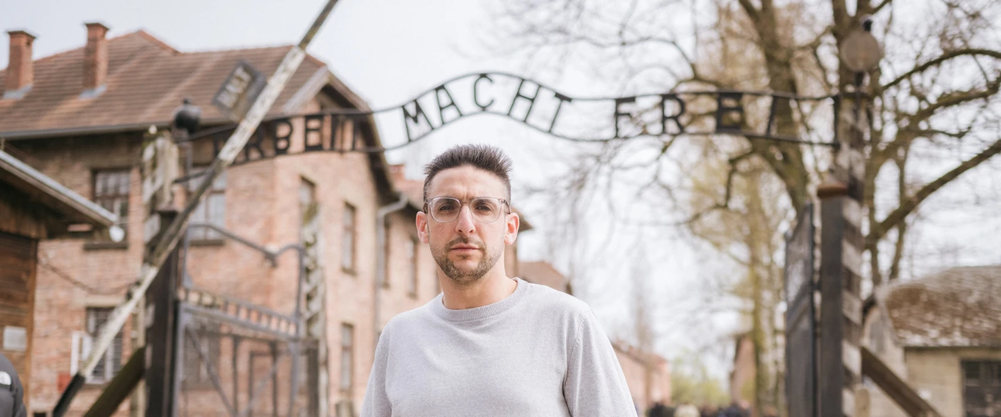 Yoni Finlay, a survivor of the 2025 Yom Kippur terrorist attack on Heaton Park Synagogue in Manchester, at the entrance to the Auschwitz concentration camp site in Poland, April 13, 2026. Credit: Blake Ezra Photography.