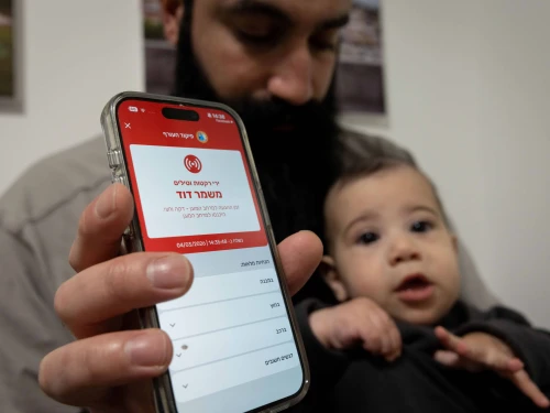 A man holding a baby shows a missile alert notification on her mobile phone as residents take cover indoors following missile fire from Iran toward Israel, in Mishmar David, March 4, 2026. Photo by Nati Shohat/Flash90.