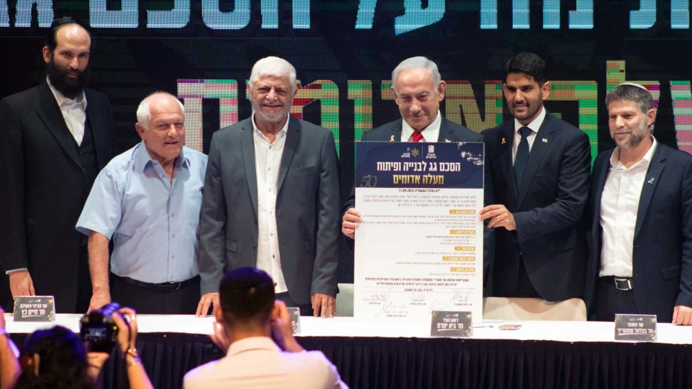 Israeli Prime Minister Benjamin Netanyahu holds up the umbrella agreement at a signing ceremony at the Maale Adumim Cultural Center. Also on stage (from left) are Ministry of Construction and Housing Director-General Yehuda Morgenstern, Housing Minister Haim Katz, former Maale Adumim Mayor Benny Kashriel, current Maale Adumim Mayor Guy Yifrach, and Finance Minister Bezalel Smotrich, Sept. 11, 2025. Photo by David Isaac.