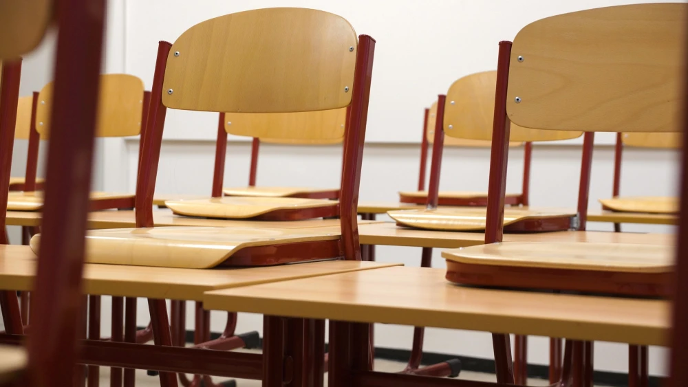 Chairs propped up on desks in an empty classroom. Credit: Taken/Pixabay.