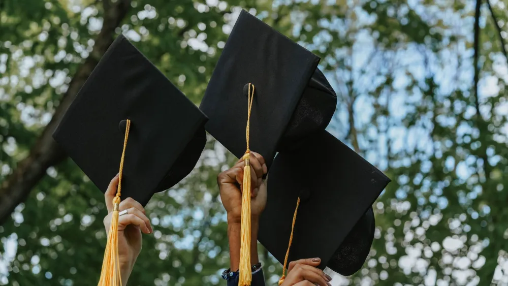 Individuals holding up graduation caps. Credit: olia danilevich/Pexels.
