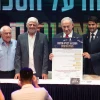 Israeli Prime Minister Benjamin Netanyahu holds up the umbrella agreement at a signing ceremony at the Maale Adumim Cultural Center. Also on stage (from left) are Ministry of Construction and Housing Director-General Yehuda Morgenstern, Housing Minister Haim Katz, former Maale Adumim Mayor Benny Kashriel, current Maale Adumim Mayor Guy Yifrach, and Finance Minister Bezalel Smotrich, Sept. 11, 2025. Photo by David Isaac.
