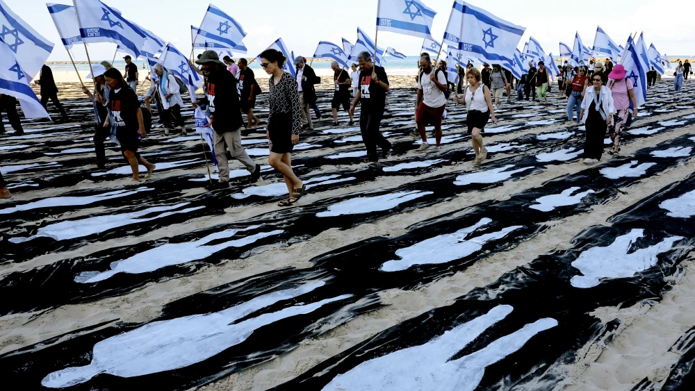 People carrying Israeli flags walk through a commemorative installation set up on the beach in Tel Aviv to mark the third anniversary of Hamas's October 7 attack on Israel, on Oct. 7, 2026. Photo by Jack Guez / AFP via Getty Images.