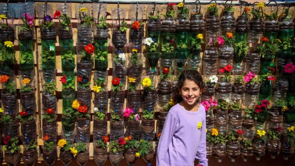 A girl stands by a wall full of flowers in plastic bottles at Amichai School in Kibbutz Yavne on March 24, 2017. Photo by Gershon Elinson/Flash90.