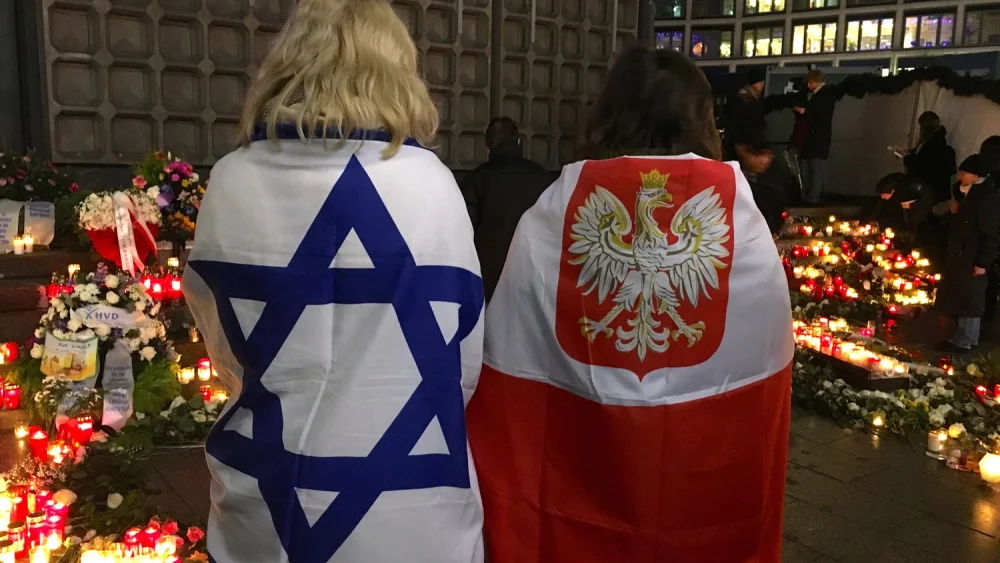 Antje Böttinger (left), wrapped in an Israeli flag, and a woman wearing a Polish flag visit a memorial to victims of the December 2016 Berlin Christmas market terror attack, Dec. 19, 2018. Credit: Orit Arfa.