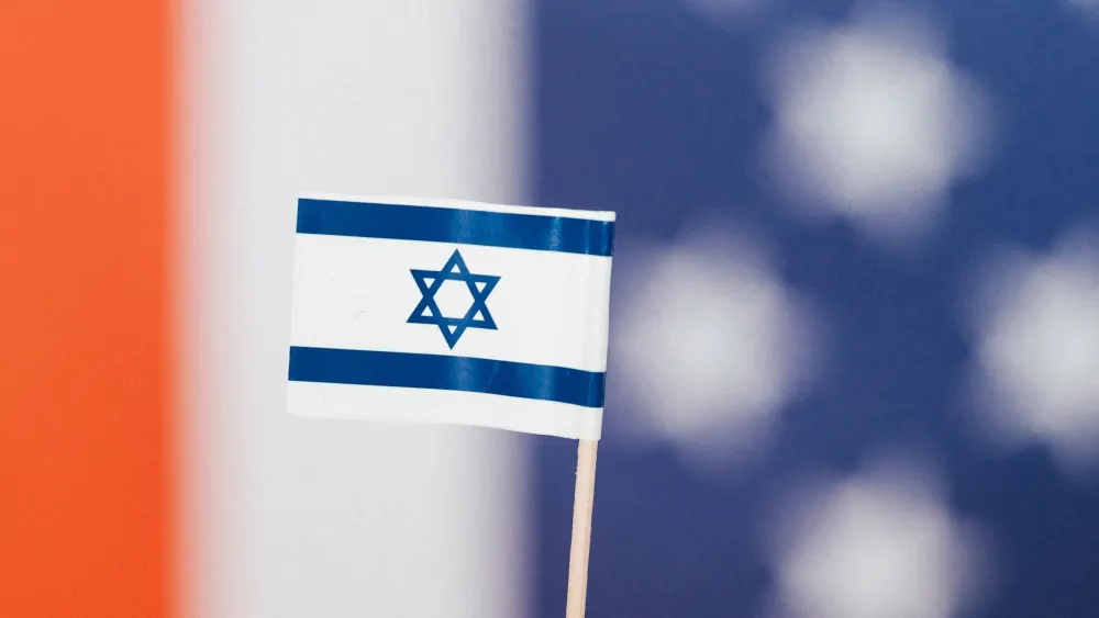 A small Israeli flag against a blurred American flag background. Credit: Kaboom Pics/Pexels.