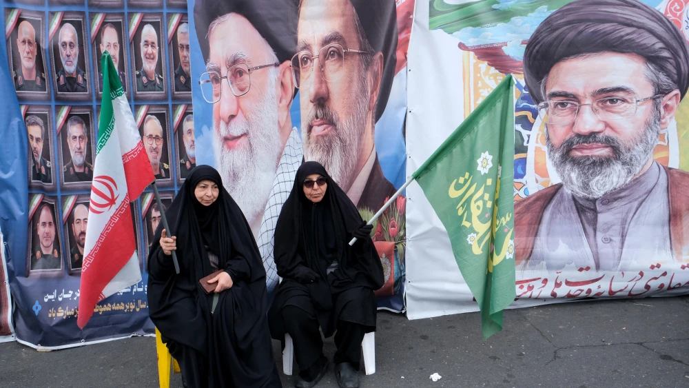 Two Iranian regime supporters sit on a bench in front of images of Ayatollah Ali Khamenei and his successor, Supreme Leader Mojtaba Khamenei, on the corner of Tehran's Revolution Square, March 28, 2026. Photo by Kaveh Kazemi/Getty Images.