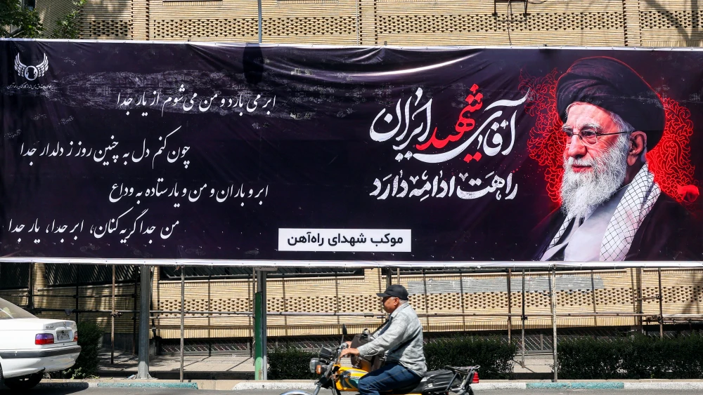 A man rides a motorcycle past a mourning banner depicting slain Iranian Supreme Leader Ali Khamenei, who was killed in the Feb. 28 opening strike of the U.S.-Israeli war against the Islamic Republic, in Tehran, June 30, 2026. Photo by AFP via Getty Images.