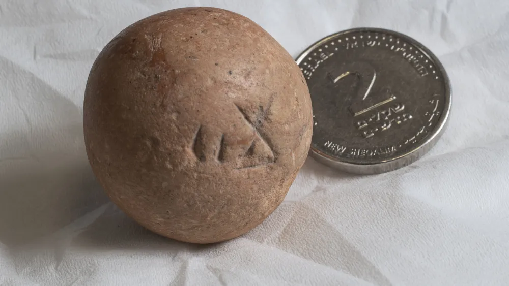 A limestone "two-shekel" weight, dating back to the Iron Age/First Temple period, discovered during excavations conducted by the Israel Antiquities Authority in conjunction with the Western Wall Heritage Foundation. It is seen here next to a modern two-shekel coin. Credit: Israel Antiquities Authority.