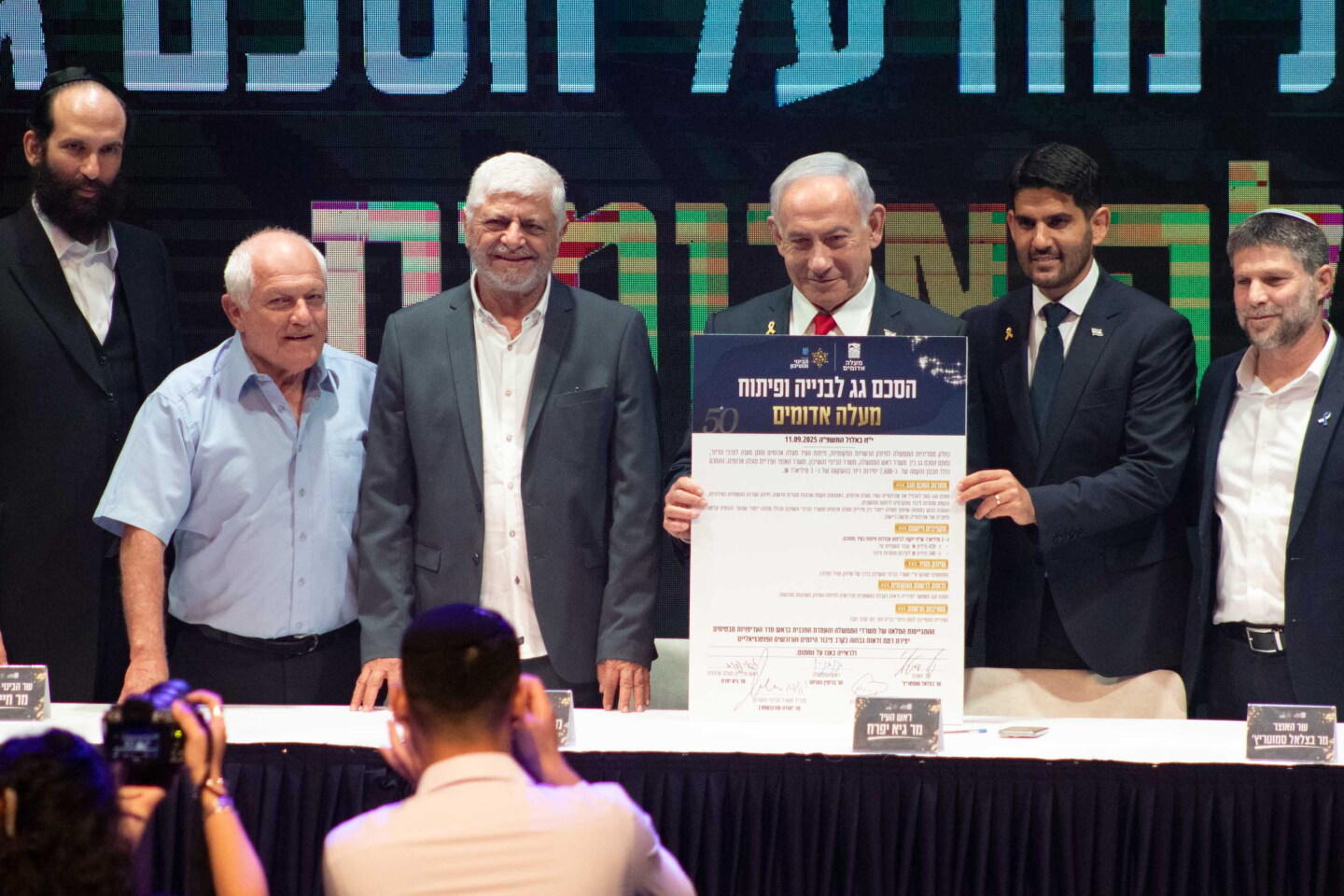Israeli Prime Minister Benjamin Netanyahu holds up the umbrella agreement at a signing ceremony at the Maale Adumim Cultural Center. Also on stage (from left) are Ministry of Construction and Housing Director-General Yehuda Morgenstern, Housing Minister Haim Katz, former Maale Adumim Mayor Benny Kashriel, current Maale Adumim Mayor Guy Yifrach, and Finance Minister Bezalel Smotrich, Sept. 11, 2025. Photo by David Isaac.
