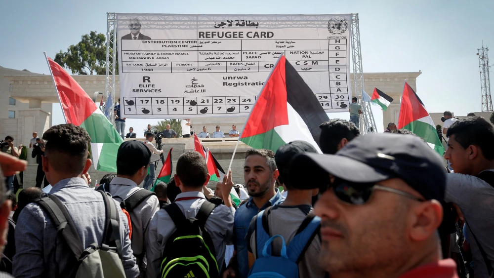 Palestinian protesters wave their national flag in front of a fabricated giant refugee card during a protest against the U.S. decision to cut U.N. funds to Palestinians in the West Bank city of Bethlehem on Sept. 26, 2018. Credit: Wisam Hashlamoun/Flash90.