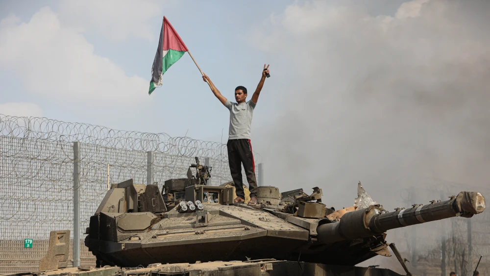 Palestinians stand next to a burning tank inside the border fence with Israel in the city of Khan Yunis in the southern Gaza Strip. Oct. 7, 2023. Photo by Yousef Mohammed/FLASH90.