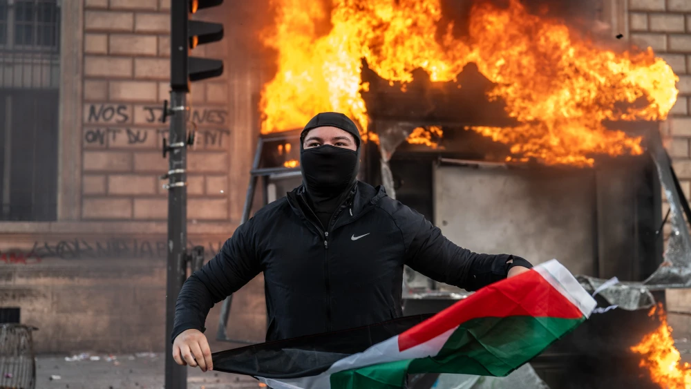 A protester holds a Palestinian flag as a bus stop burns during a demonstration at Place de Republique in Paris, France, on October 17, 2026. Photo by Guy Smallman/Getty Images.