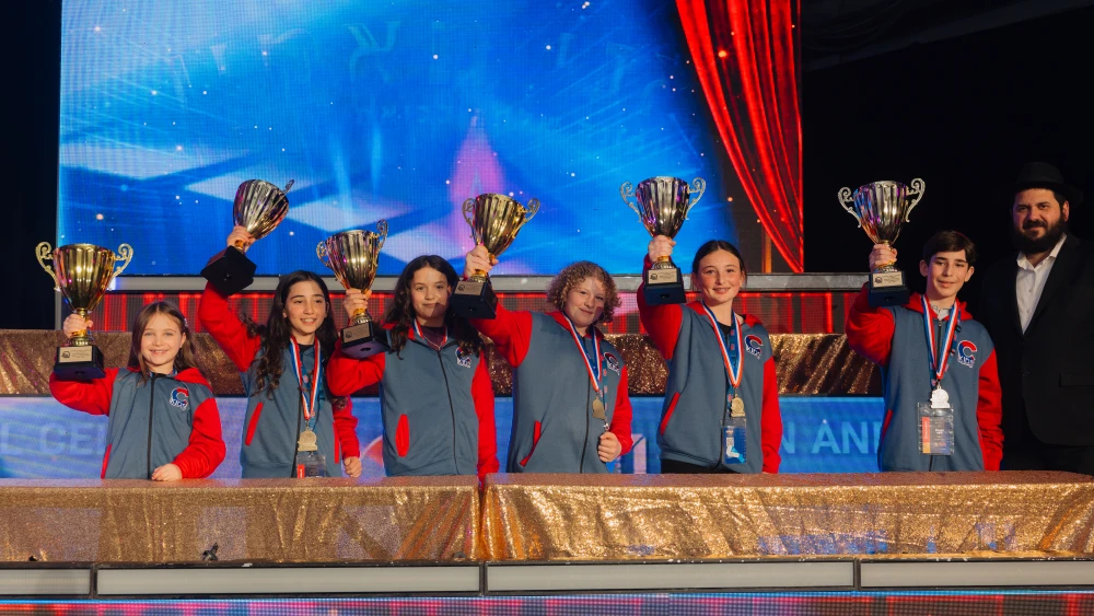 Six young champions raise their trophies at the 2026 JewQ International Jewish Knowledge Championship. L-R: Chaya (Charlotte) Henn (Grade 3, Nevada), Skylar Cohen (Grade 4, California), Zoe Shlivko (Grade 5, New York), Sylvia Fletcher (Grade 6, Arizona), Abby Mendelsohn (Grade 7, Florida), David Bain (Grade 8, Louisiana). Courtesy of Chabad Global Networks