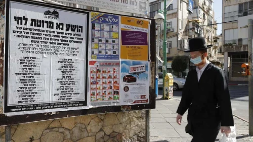 An man walks past a sign in Bnei Brak urging masking and social distancing, Oct. 16, 2020. Photo by Eitan Elhadez-Barak/TPS.