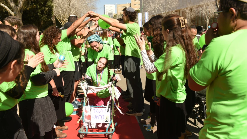 With the help of a specially-made walker and cheering staff and volunteers, an ADI resident walks the red carpet after completing the 800-meter communities track at the Jerusalem Marathon on March 17, 2023. Credit: ADI.