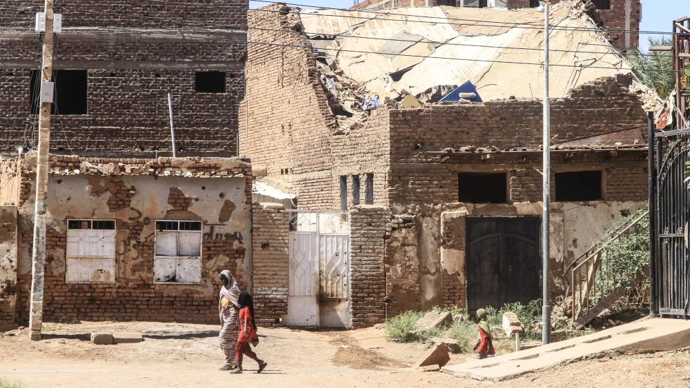 A woman and a child walk past a damaged building in the capital Khartoum on April 15, 2026, on the third anniversary of the start of war between the army and its paramilitary foes. Photo by Ebrahim Hamid/AFP via Getty Images.