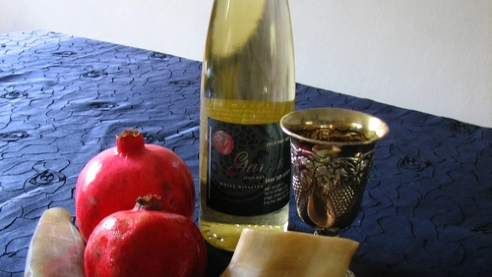 Symbols of Rosh Hashanah, the Jewish New Year, including the shofar, an apple and honey, pomegranates, wine and a silver Kiddush cup. Credit: Gilabrand via Wikimedia Commons.