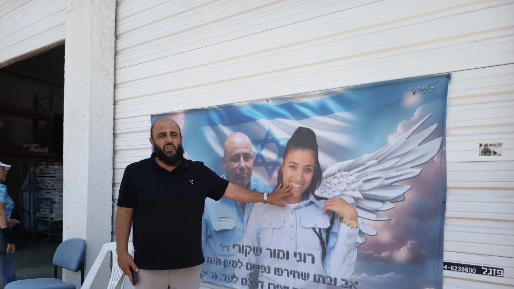 Nir Kalfa stands beside a mural at the Sderot police station memorial depicting a father and daughter, both police officers, who were killed on Oct. 7, 2023, Aug. 11, 2026. Photo by Linda Gradstein.