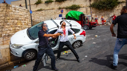An Israeli policeman fends off an angry Arab mob swarming an Israeli motorist, pelting his car with stones and driving him off the road, outside Jerusalem's Old City, May 10, 2021. Photo by Olivier Fitoussi/Flash90.