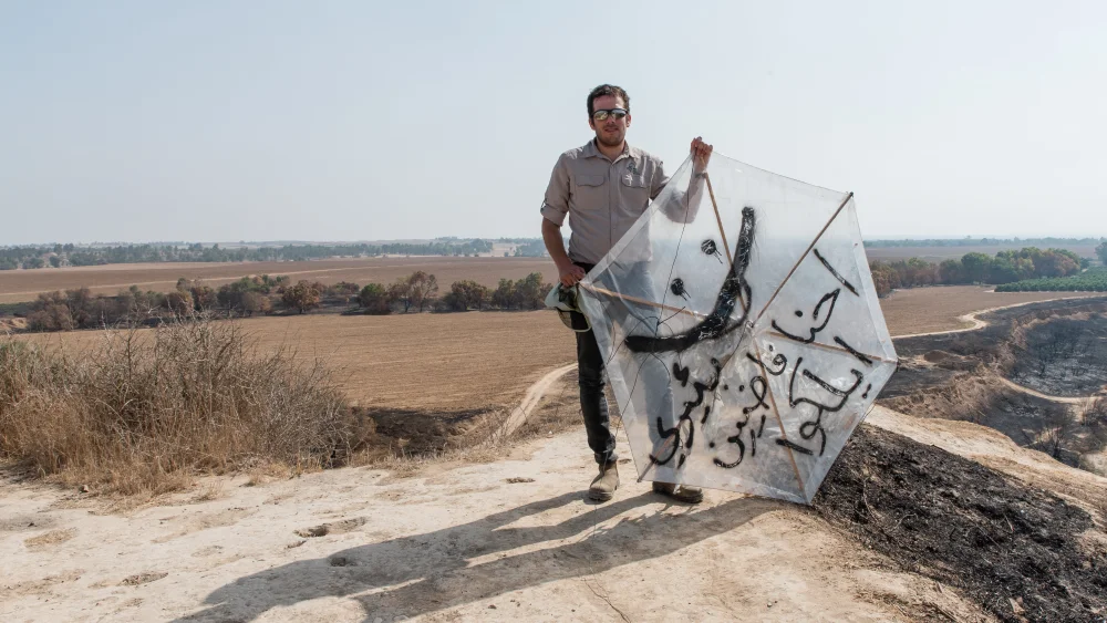 A man holds a kite from Gaza in a burnt area of Besor Stream in Tel Gama, near Kibbutz Re’im, near the border with the Gaza Strip, on July 25, 2018. Photo by Dario Sanchez/Flash90.