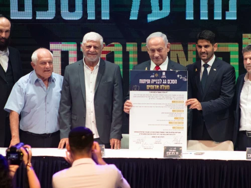 Israeli Prime Minister Benjamin Netanyahu holds up the umbrella agreement at a signing ceremony at the Maale Adumim Cultural Center. Also on stage (from left) are Ministry of Construction and Housing Director-General Yehuda Morgenstern, Housing Minister Haim Katz, former Maale Adumim Mayor Benny Kashriel, current Maale Adumim Mayor Guy Yifrach, and Finance Minister Bezalel Smotrich, Sept. 11, 2025. Photo by David Isaac.