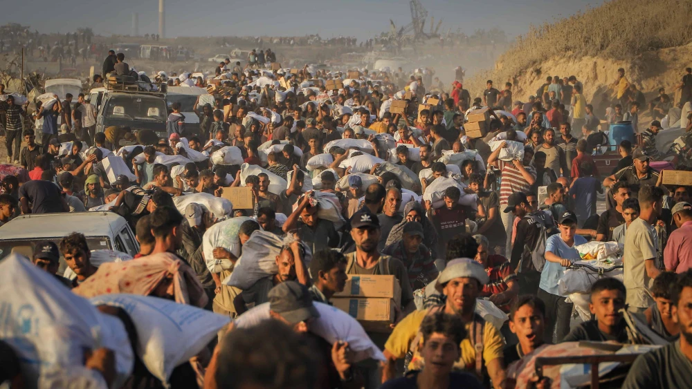 Palestinians carry food parcels and supplies from aid trucks near the Zikim border crossing between Israel and Beit Lahia, in the northern Gaza Strip, Aug. 18, 2025. Photo by Khalil Kahlout/ Flash90.