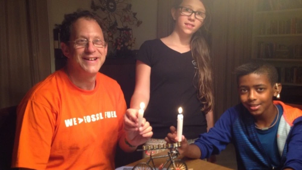 Solar-power pioneer Yosef Abramowitz (left) pictured with two of his five children, Ashira and Zamir, as the family uses its bicycle-shaped Hanukkah menorah. Credit: Courtesy Yosef Abramowitz.