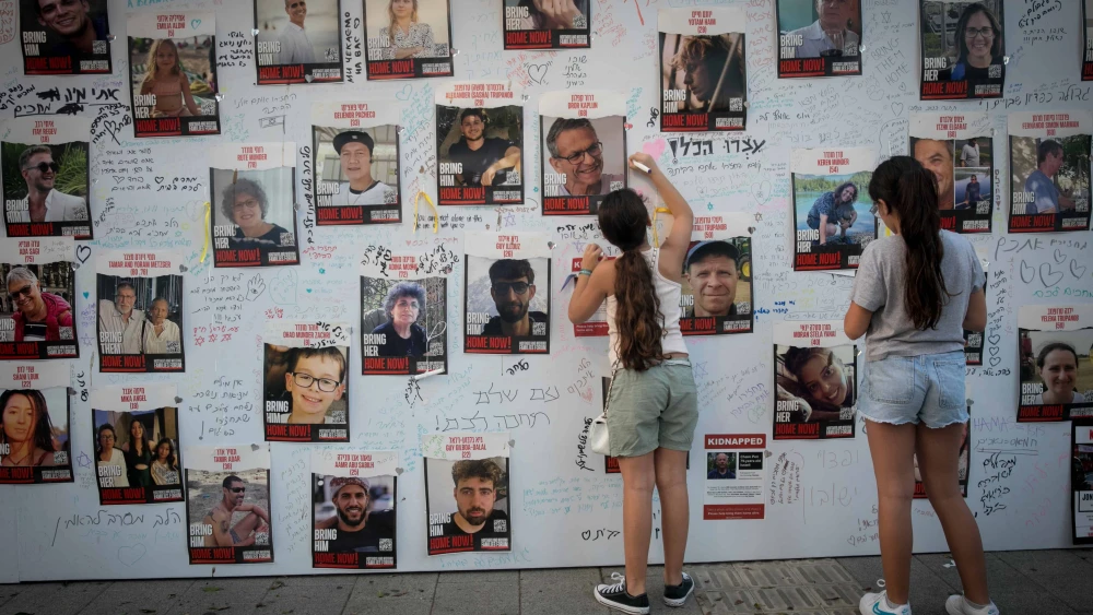 Girls write a message on posters showing photos of Israelis held kidnapped by Hamas terrorists in Gaza outside the Tel Aviv Museum of Art on Oct. 28, 2023. Photo by Miriam Alster/Flash90.