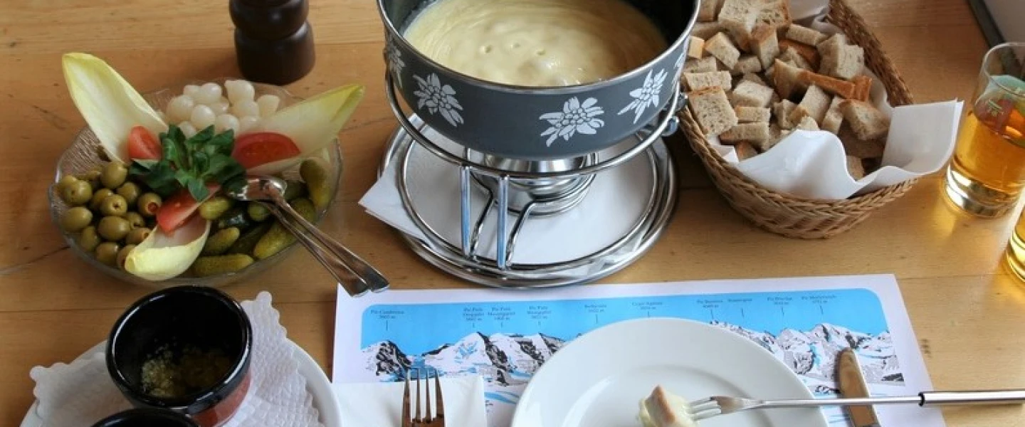 A full cheese fondue set in Switzerland. Apart from pieces of bread to dip into the melted cheese, it comes with side servings of kirsch, raw garlic, olives, pickled gherkins and baby onions. Credit: Wikimedia Commons.
