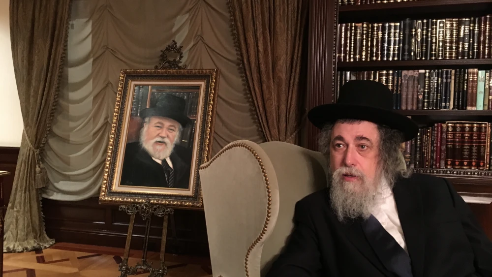 Rabbi Isaac Schapira, founder of the European Jewish Cemeteries Initiative, sitting with a portrait of his late father, Rabbi Avraham Schapira. Credit: Howard Blas.
