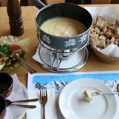 A full cheese fondue set in Switzerland. Apart from pieces of bread to dip into the melted cheese, it comes with side servings of kirsch, raw garlic, olives, pickled gherkins and baby onions. Credit: Wikimedia Commons.