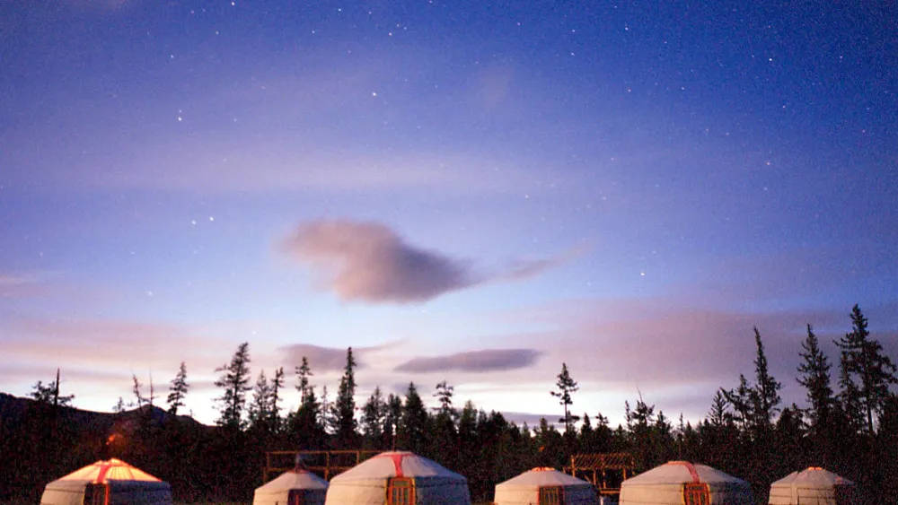 The sun goes sets on a mountain ridge as tourists light the furnaces in their Gers, or traditional Mongolian tents, at a tourist Ger camp on northern Mongolia's alpine Khovsgol Lake on July 9, 2000. Photo credit should read STEPHEN SHAVER/AFP via Getty Images.
