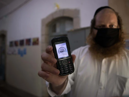 A teacher holds up his cellular phone, certificating that it is a "kosher" one, at the entrance to an ultra-Orthodox school in Jerusalem, May 6, 2020. Photo by Nati Shohat/Flash90.