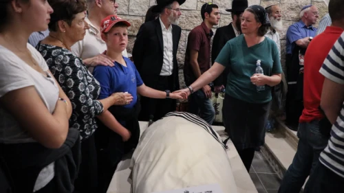 Ari Fuld's wife, Miriam, and son hold hands over his enshrouded body, wrapped in a tallit and awaiting burial at the Kfar Etzion cemetery in Judea. Photo by Gershon Elinson/Flash90.