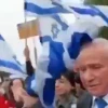 Israeli Agriculture Minister Avi Dichter is hit on the head with a flag during a protest against the government's judicial reform program, March 23, 2023. Source: Screenshot.