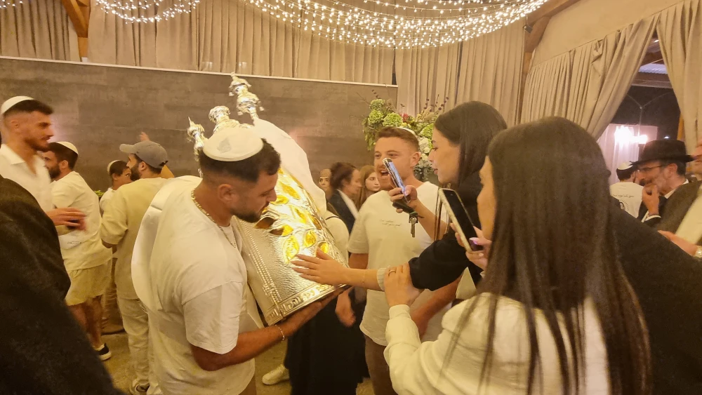 Celebrants at the David Castle event hall in Jerusalem photograph the names of friends murdered by Gazan terrorists on Oct. 7, 2023, engraved on a Torah scroll case, Oct. 3, 2026. Photo by Sharon Altshul.
