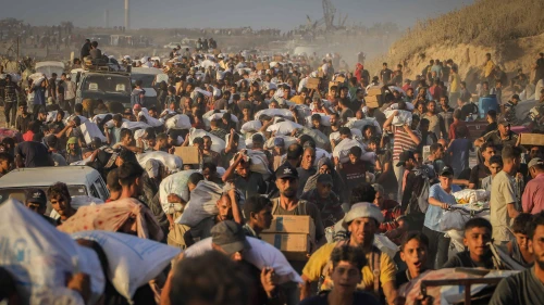 Palestinians carry food parcels and supplies from aid trucks near the Zikim border crossing between Israel and Beit Lahia, in the northern Gaza Strip, Aug. 18, 2025. Photo by Khalil Kahlout/ Flash90.