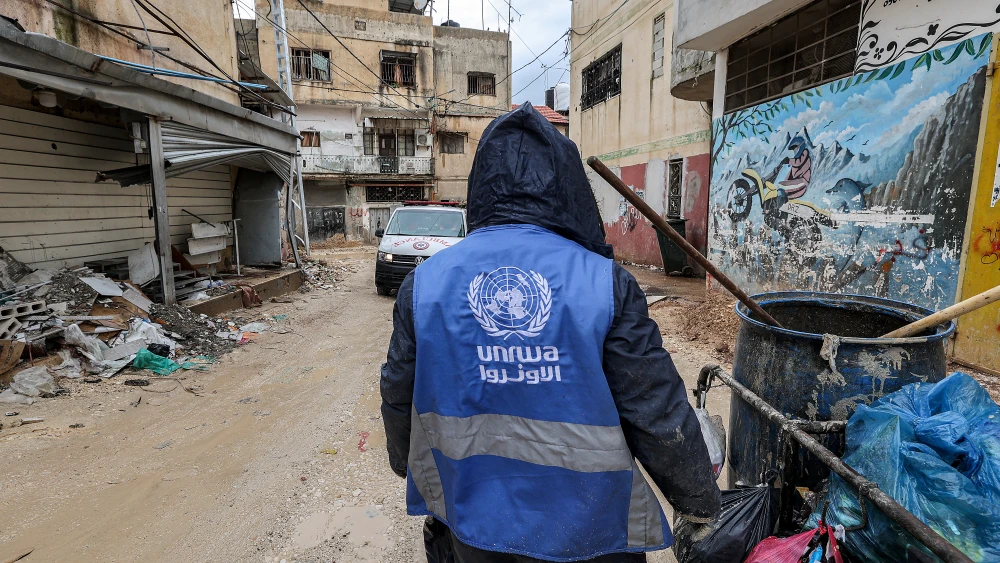 A man collects trash while wearing a jacket bearing the logo of the United Nations Relief and Works Agency, along a street in Jenin,northern Samaria, on Jan. 30, 2024. Photo by Jaafar Ashtiyeh/AFP via Getty Images.