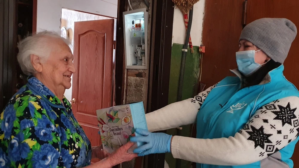 Gallina Rashba receives a box of matzah for Passover from a JDC volunteer. Credit: JDC.