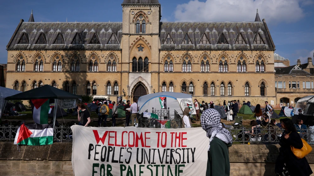 A passerby with the head covered with a keffiyeh walks past a banner reading "Welcome to the people's university for Palestine" at Oxford University, in Oxford, eastern England on May 7, 2024. Photo by Adrian DENNIS / AFP via Getty Images.