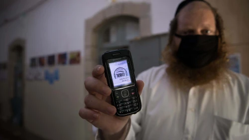 A teacher holds up his cellular phone, certificating that it is a "kosher" one, at the entrance to an ultra-Orthodox school in Jerusalem, May 6, 2020. Photo by Nati Shohat/Flash90.