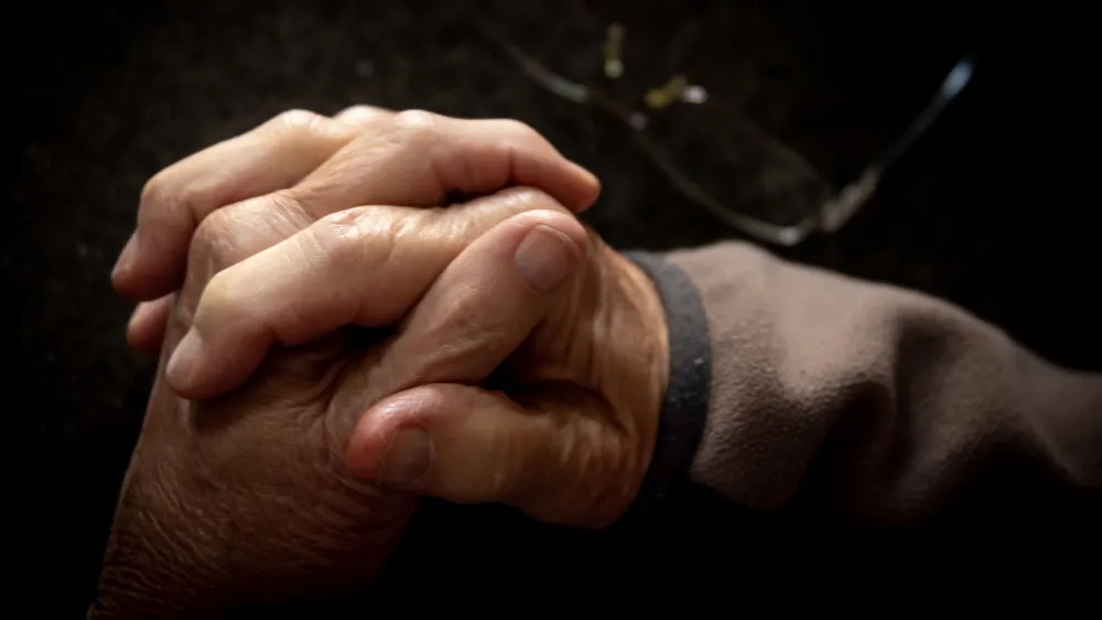 Elderly hands on a table next to a pair of glasses. Credit: Magda Ehlers/Pexels.