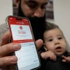 A man holding a baby shows a missile alert notification on her mobile phone as residents take cover indoors following missile fire from Iran toward Israel, in Mishmar David, March 4, 2026. Photo by Nati Shohat/Flash90.