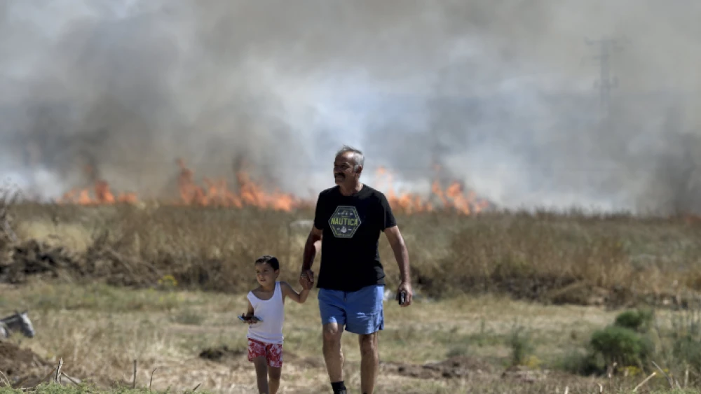 An Israeli man and child near a fire caused by shrapnel from a rocket fired from the Gaza Strip, wounding four, in Lakhish Regional Council on May 13, 2021. Photo by Gili Yaari /Flash90.