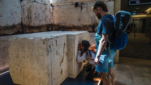 Shelly Sarah, a 22 year old Israeli from Hadera, stops at the Western Wall stone on display at Israel's Ben-Gurion International airport before a trip to Thailand as her boyfriend looks on, March 25, 2025. Credit: Rina Castelnuovo.