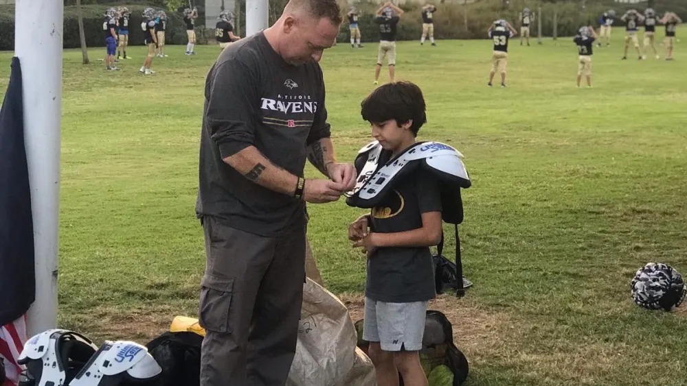 Erez Lustig, founder of “Young Champions” helps a kid with his shoulder pads. Credit: Courtesy.